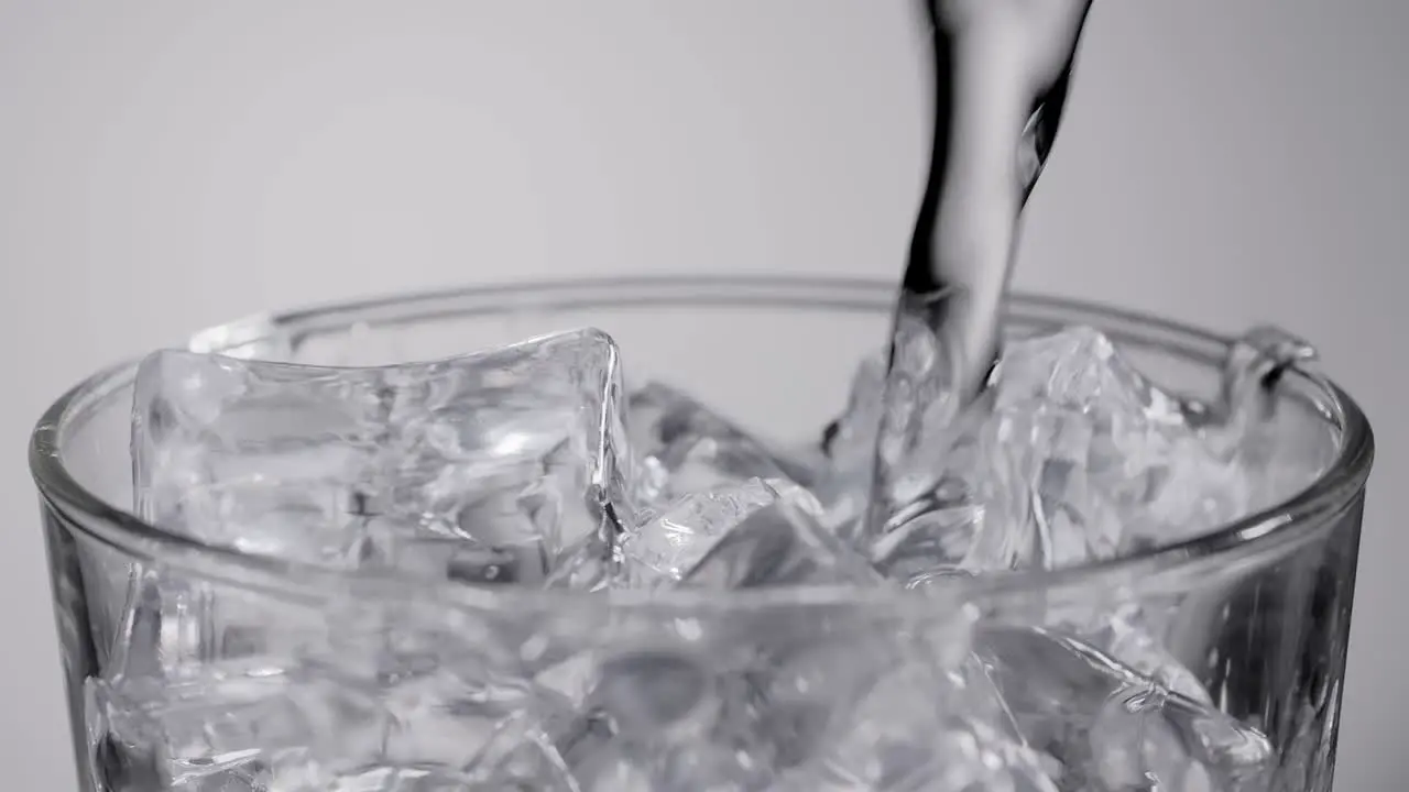 Close up slow motion water pouring into glass with ice cubes