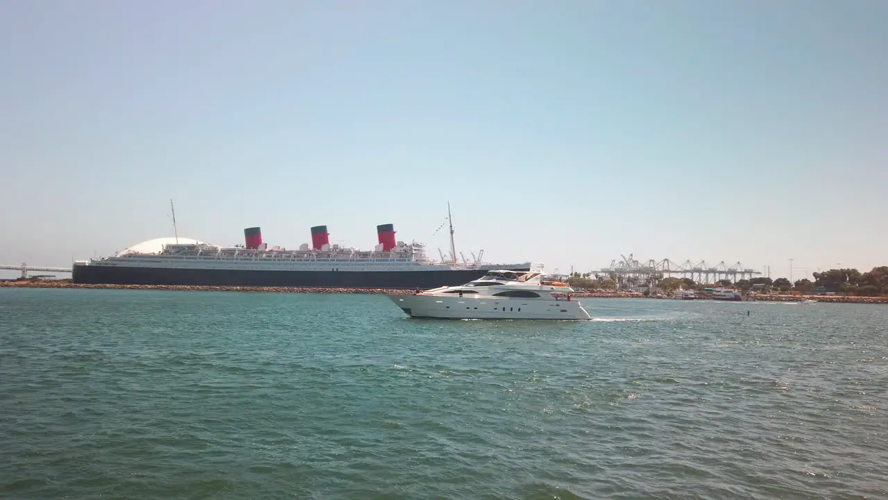 Huge private yacht passes through port entrance with giant cruise ship and Queen Mary in the background