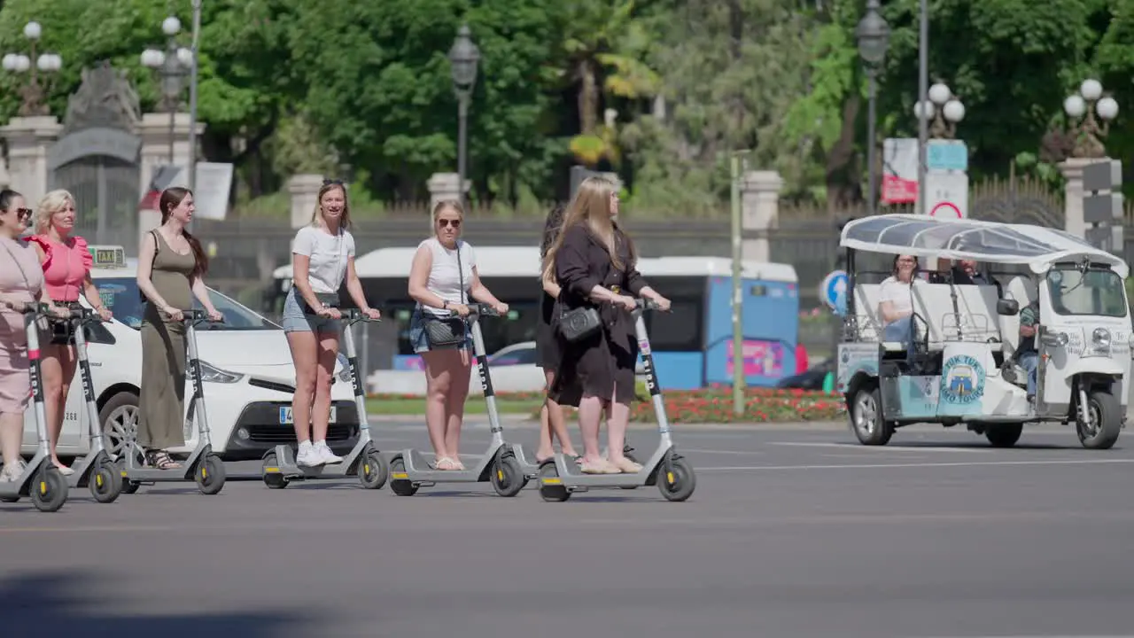 Slow motion scene where teenage girls drive through traffic on electrical scooters