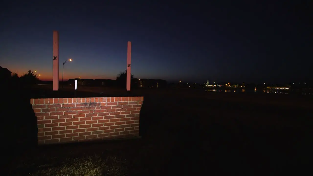 A few cars speed past blank lit up sign at night next to road near sunset