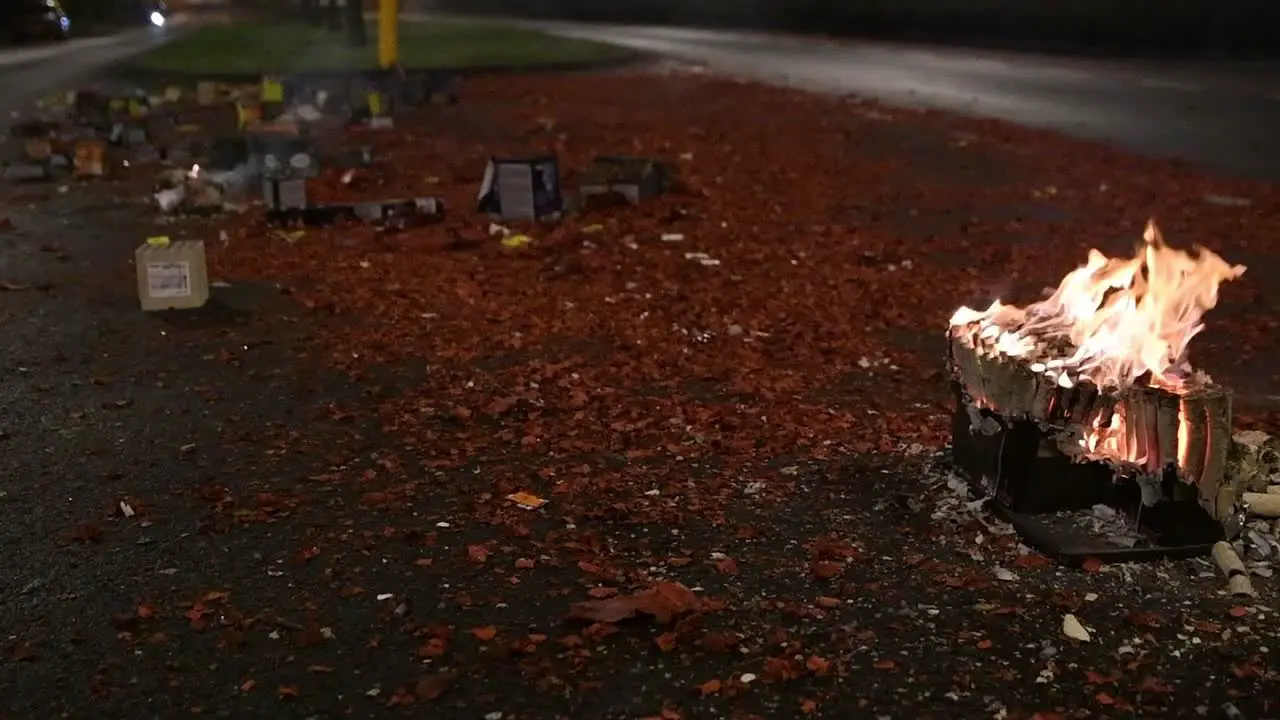 Slow motion fire burning from fireworks on debris-covered road at night