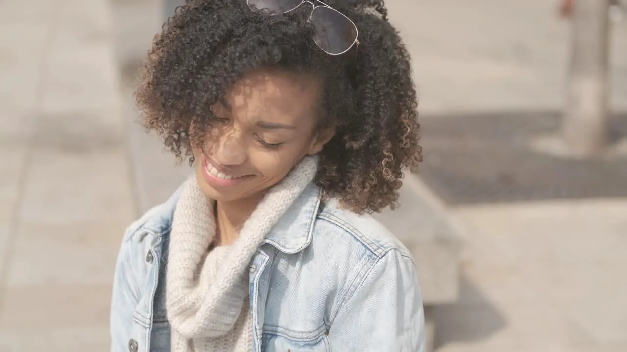 Beautiful girl with afro haircut sitting on bench at city street