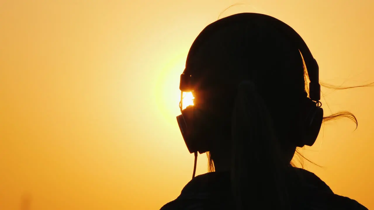 Rear View Of A Child With Headphones Listening To Music And Admiring The Sunset And A Big Orange Sky