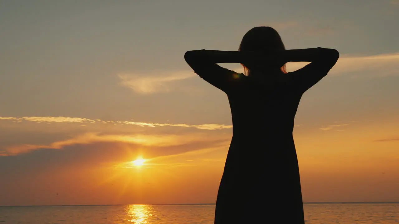 A Woman Admires The Beautiful Sky Where The Sun Sets Stands Near The Sea