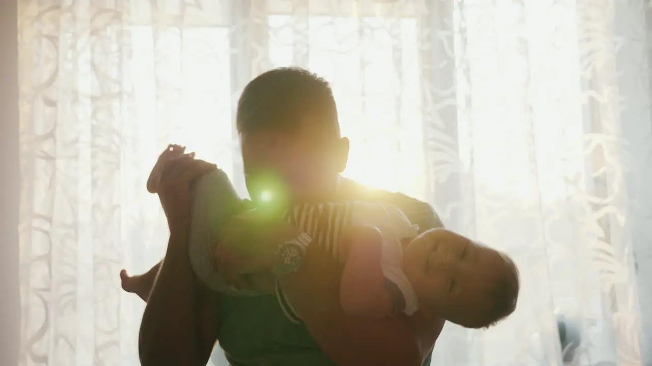 A Healthy Young Father Plays With His 1 Year Old Son Standing By The Window At Sunset Slow Motion Vi