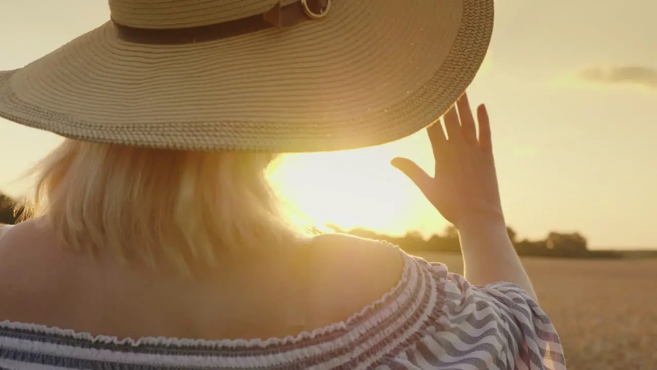 A Young Woman In A Hat Looks At The Sunset Over The Wheat Field 1