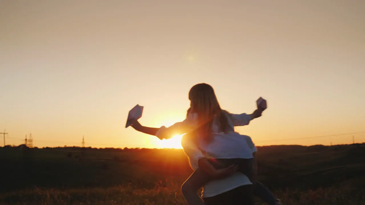 The Girl Is Sitting On Her Mother's Shoulders Playing With Paper Airplanes A Happy Family 4K Video