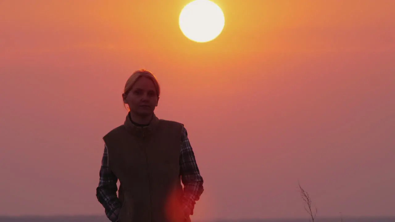 A Woman Walks Toward The Camera A Large Red Sun Shines From Behind