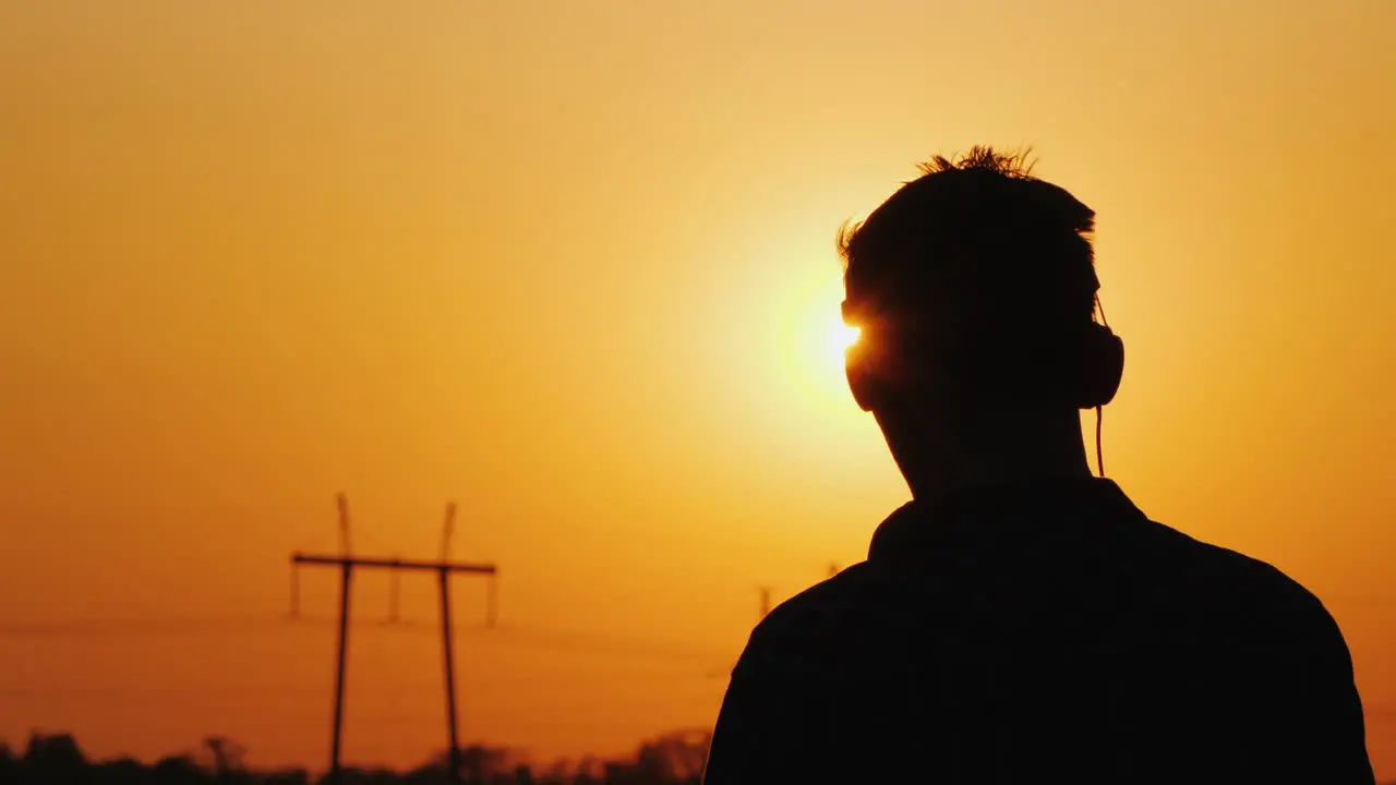 Teenager In Headphones Listening To Music Looking At A Beautiful Sunset Over The City View From Behi