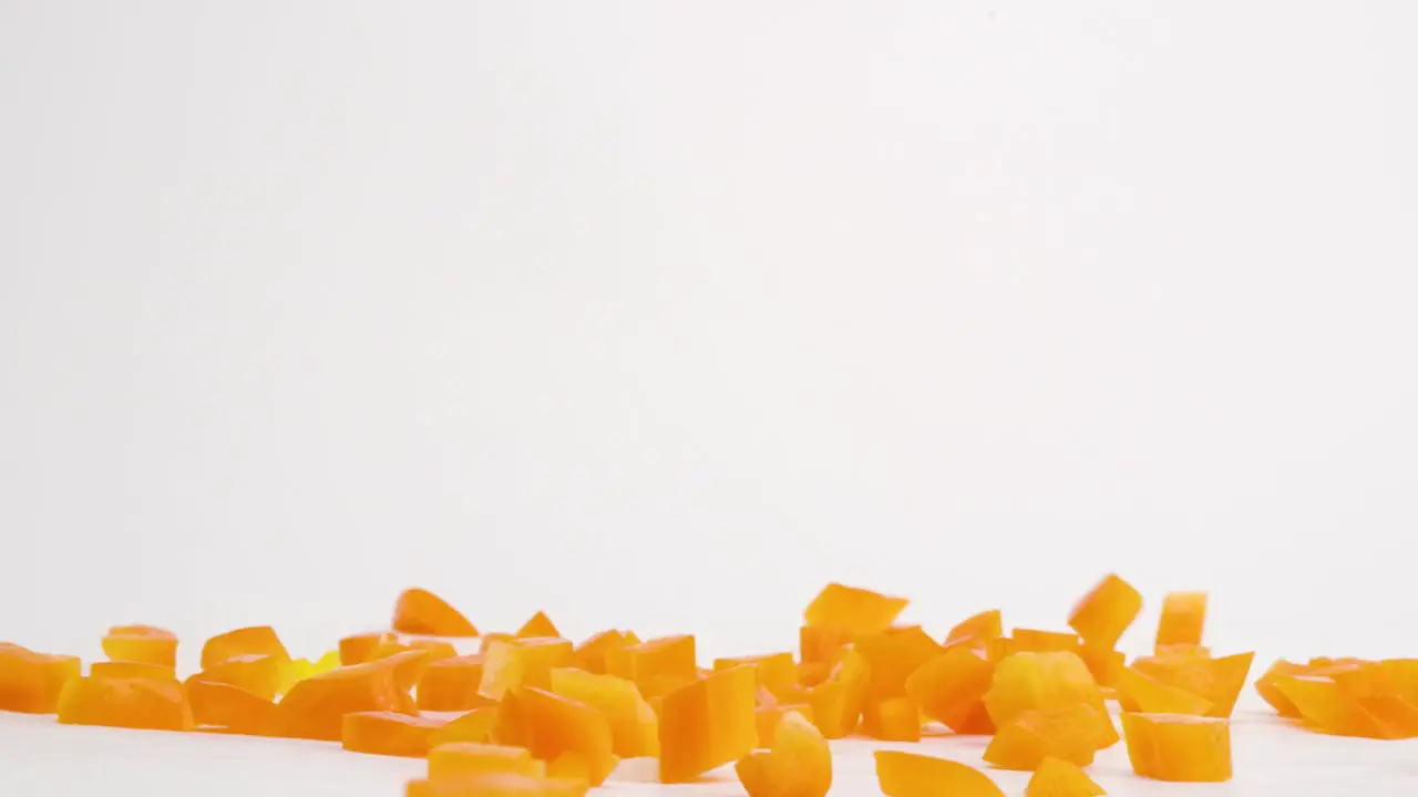 Diced cubed bright orange bell pepper vegetable pieces falling onto white table top and bouncing into a pile in slow motion