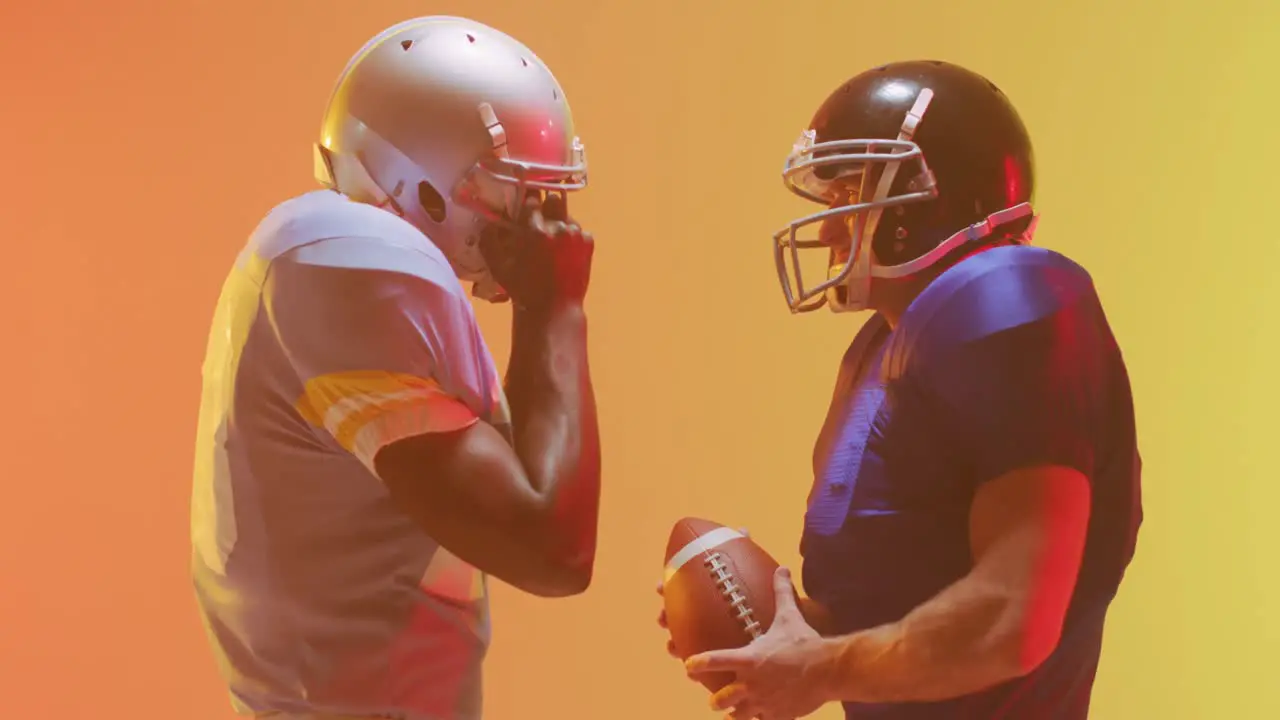 Video of diverse american football players with ball over yellow to orange background