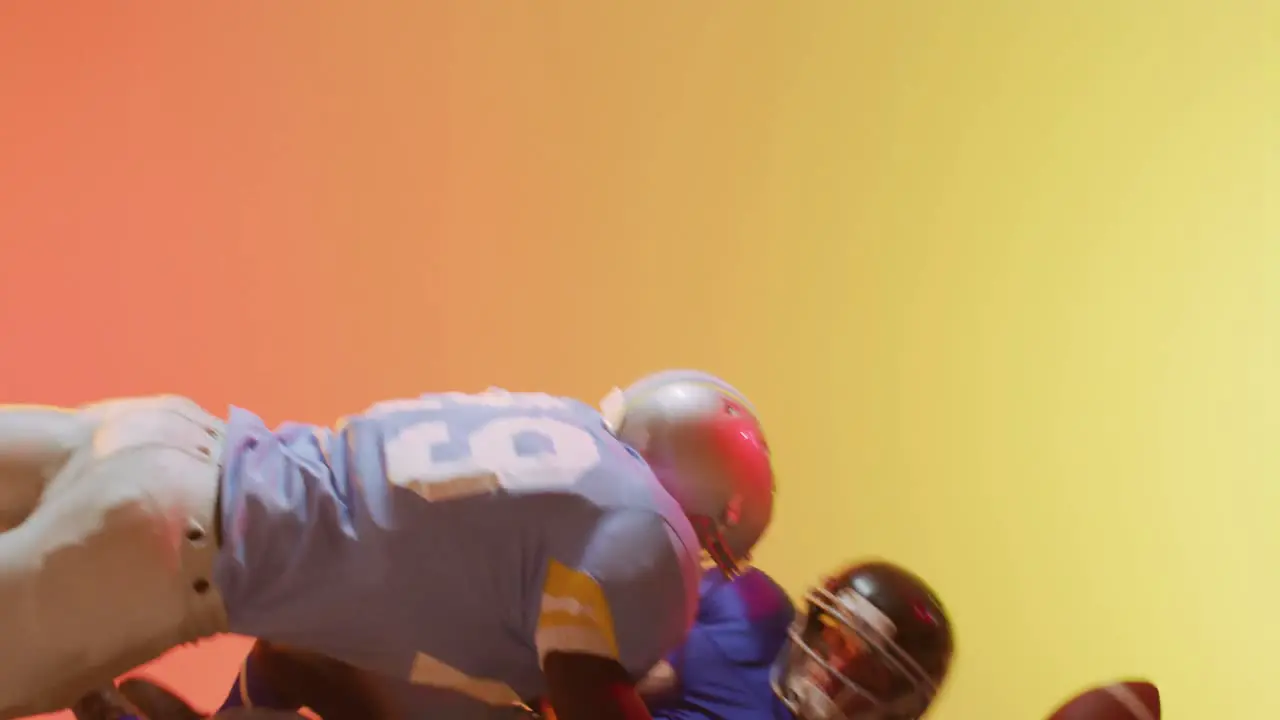 Video of diverse american football players tackling with ball over yellow to orange background