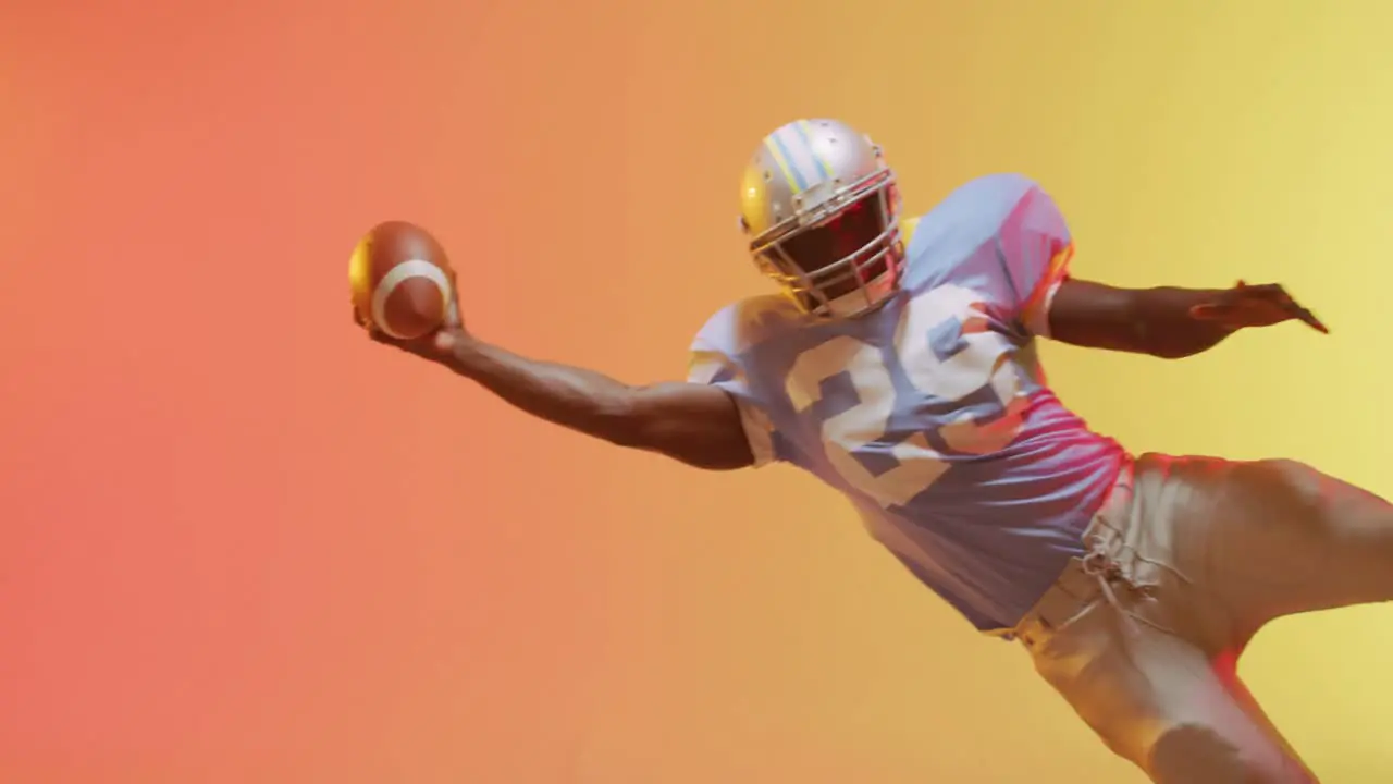 Video of african american american football player with ball over yellow to orange background