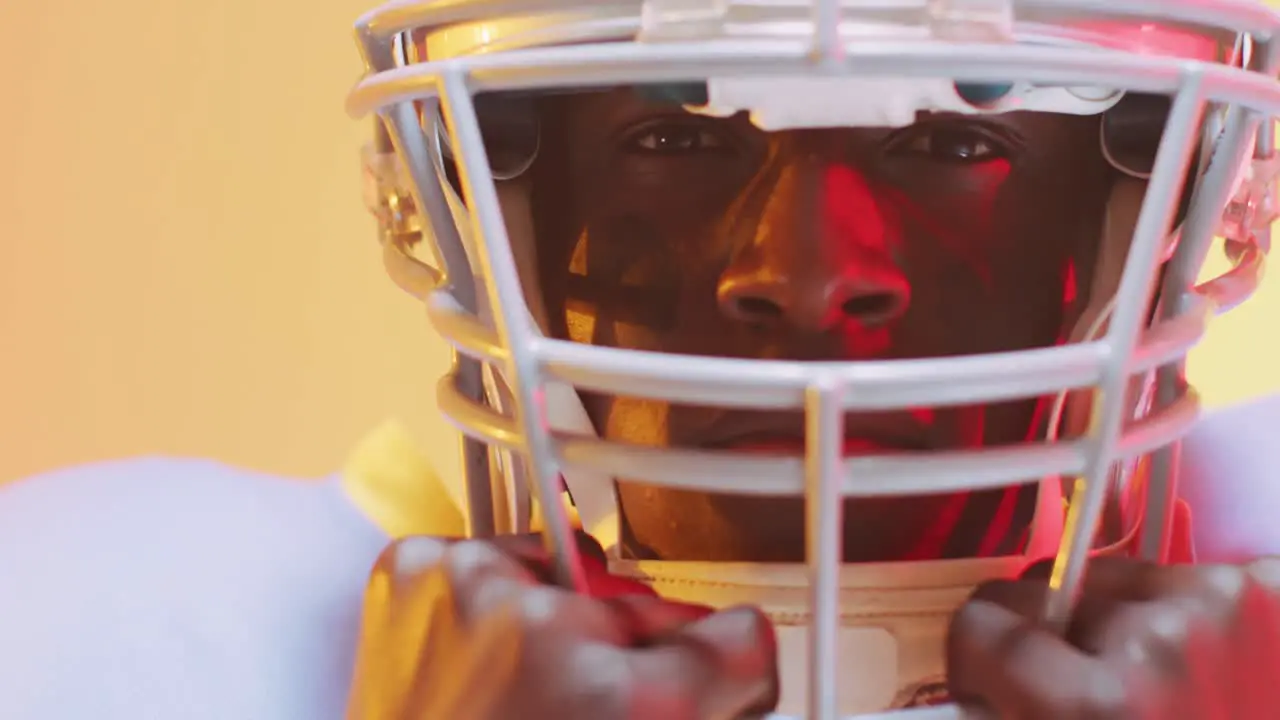 Video of african american american football player in helmet over yellow to orange background