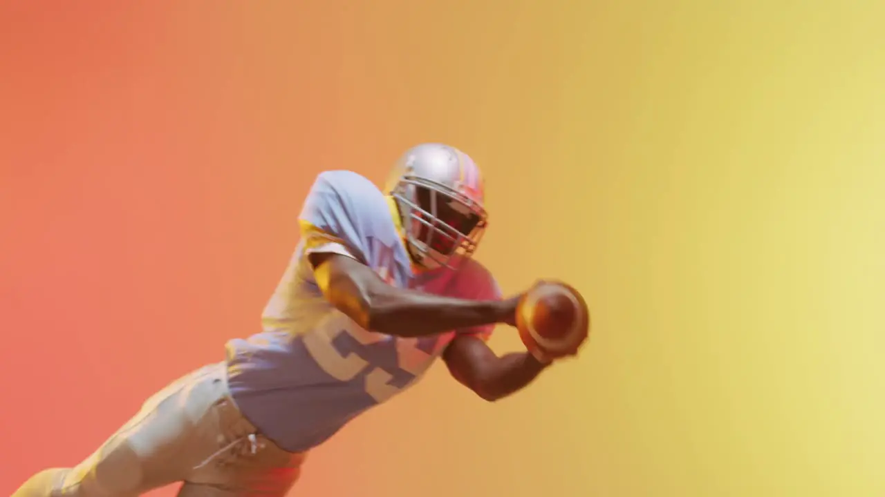 Video of african american american football player catching ball over yellow to orange background