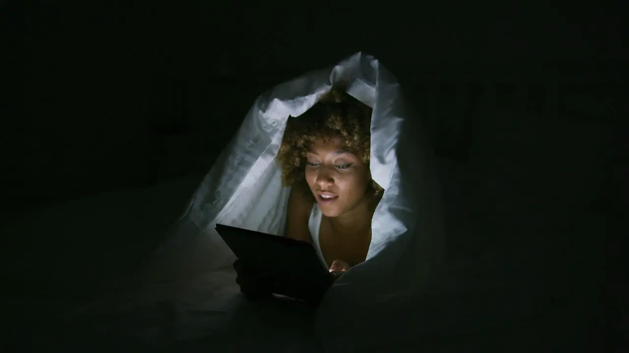 Excited woman under blanket with tablet