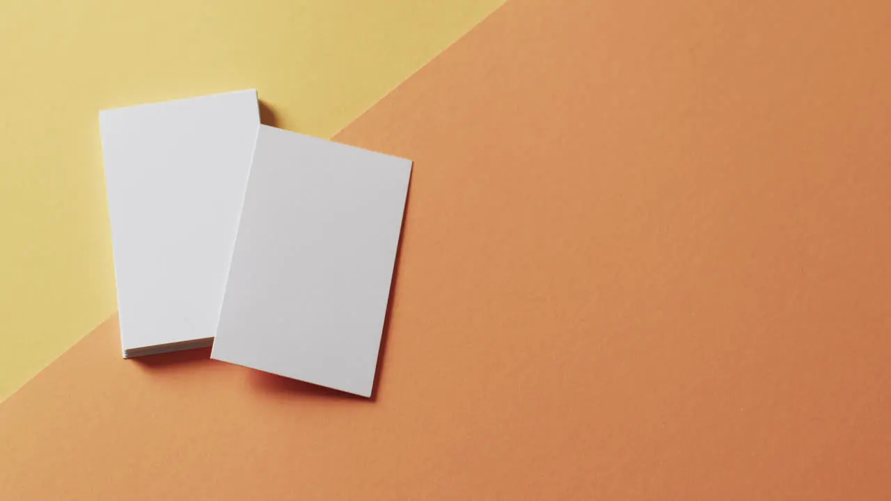 Overhead view of blank white business cards on yellow and orange background copy space slow motion