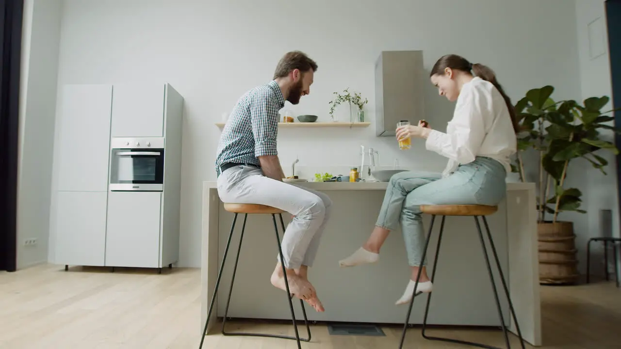 Happy Couple Chatting And Having Lunch Together Sitting On Stool In A Modern Kitchen