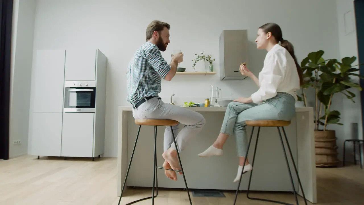 Loving Couple Chatting And Having Lunch Together Sitting On Stool In A Modern Kitchen