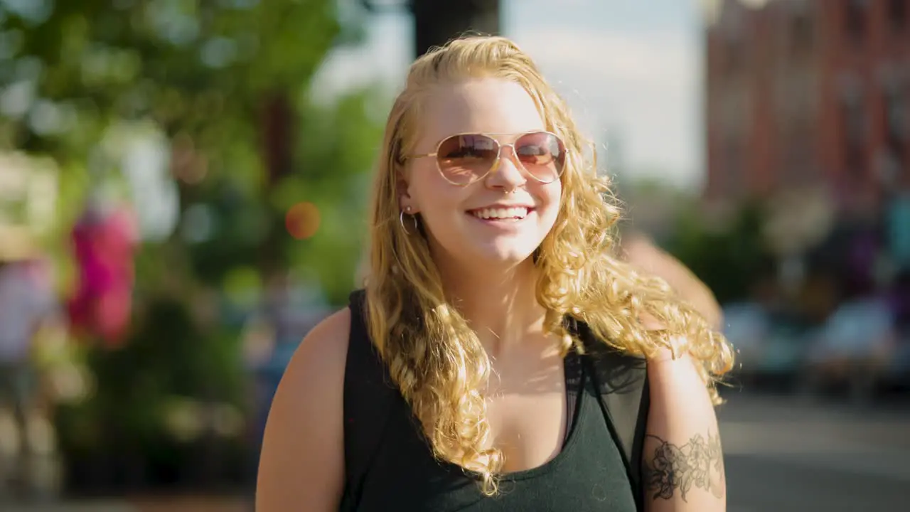 Girl with sunglasses smiles at the camera while walking through a crosswalk downtown