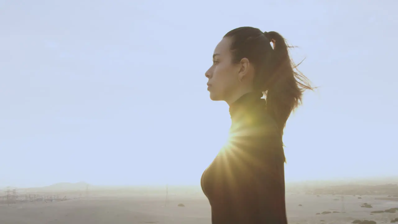 Beautiful woman in profile dressed in black and with tied hair looks straight ahead in the middle of the desert at sunset against the sun