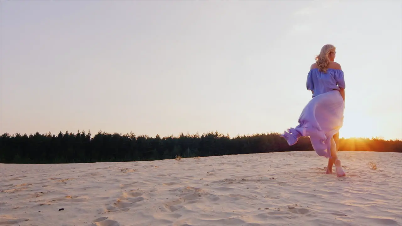 A Slender Woman In A Light Blue Dress Standing On The Beach At Sunset The Wind Plays With Her Dress