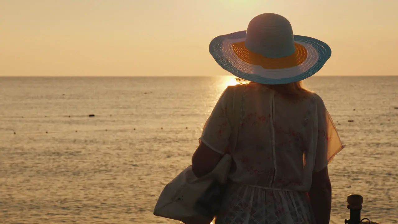 A Slender Tourist Meets The Dawn On The Sea With A Bag On Her Shoulder And A Broad-Brimmed Hat On He