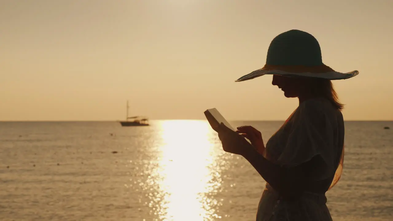 Silhouettes A Young Woman In A Wide-Brimmed Hat That Uses A Tablet Against The Backdrop Of A Beautif