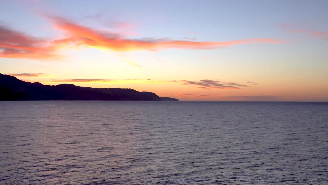 Slow tilt up over beautiful ocean sunrise with mountain silhouette