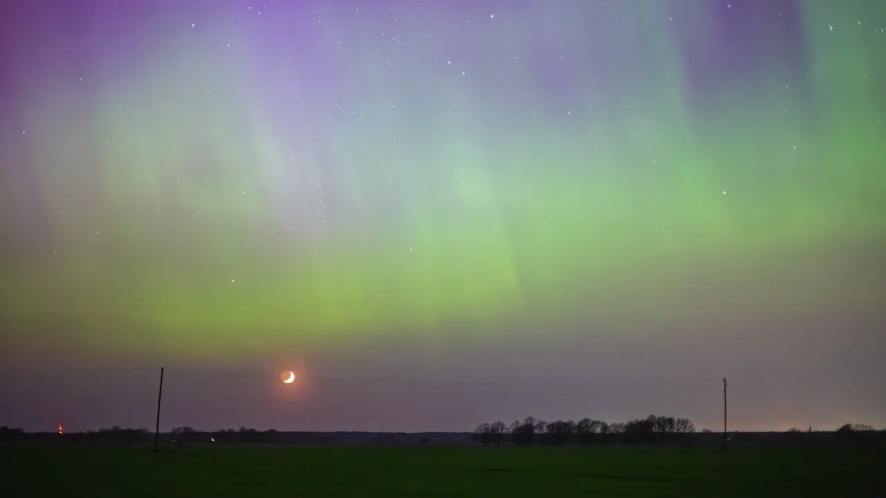 Aurora borealis lights the nighttime sky as the crescent moon sets below the horizon time lapse