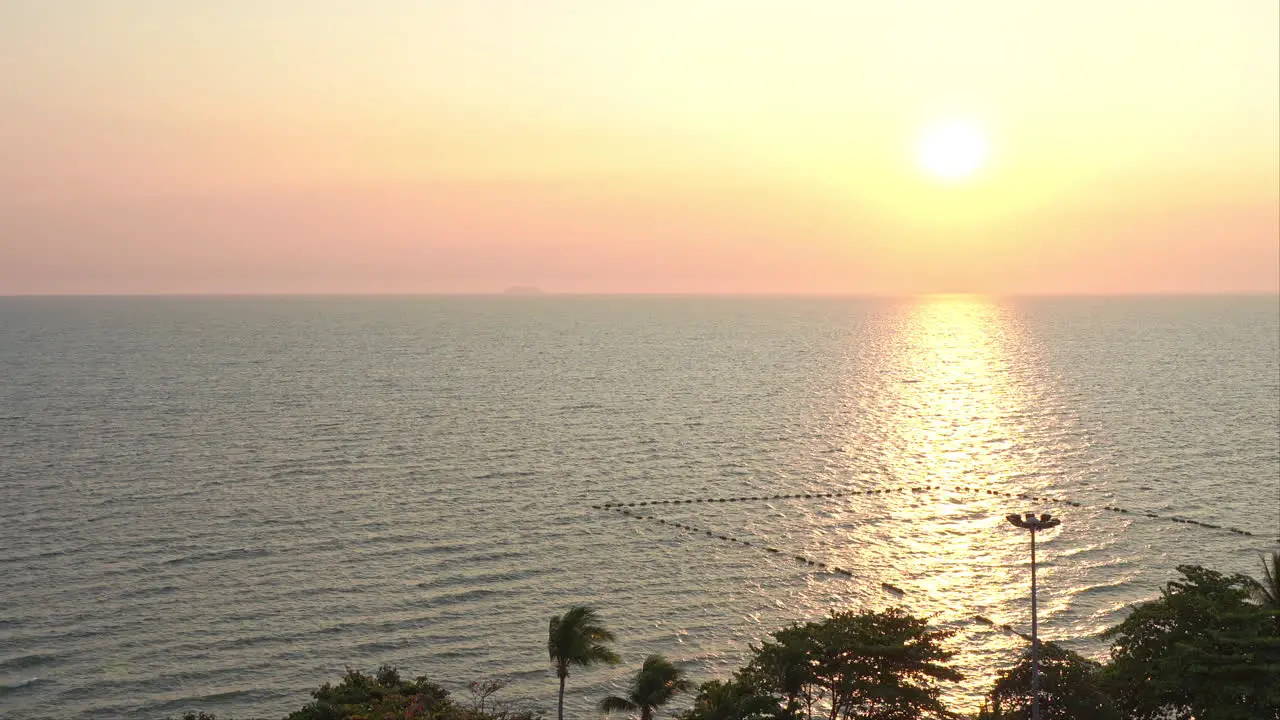 Pink colorful Seafront sunset with sunlight reflecting in water surface palm treetops in foreground Thailand