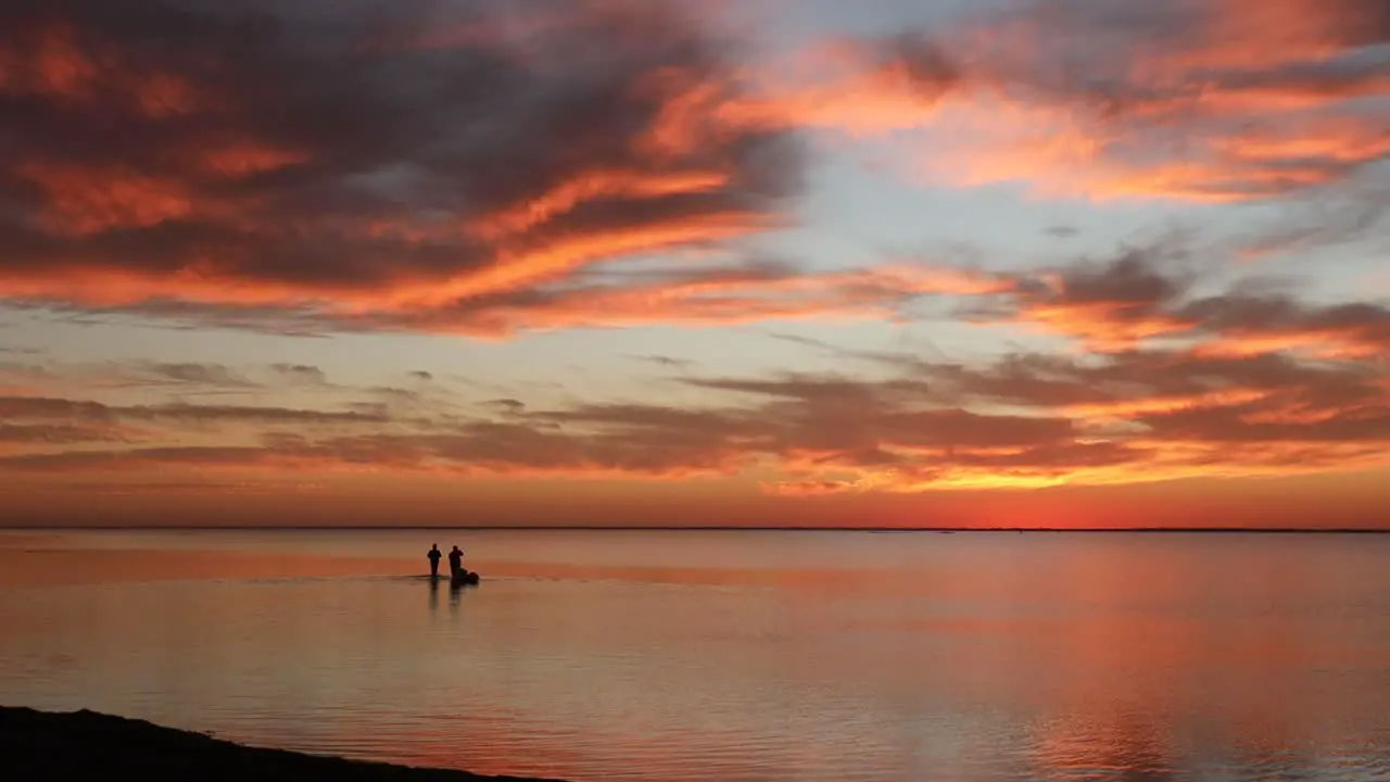 Two people wade into tranquil Laguna Madres estuary while towing fishing gear in a kayak during a gorgeous sunset