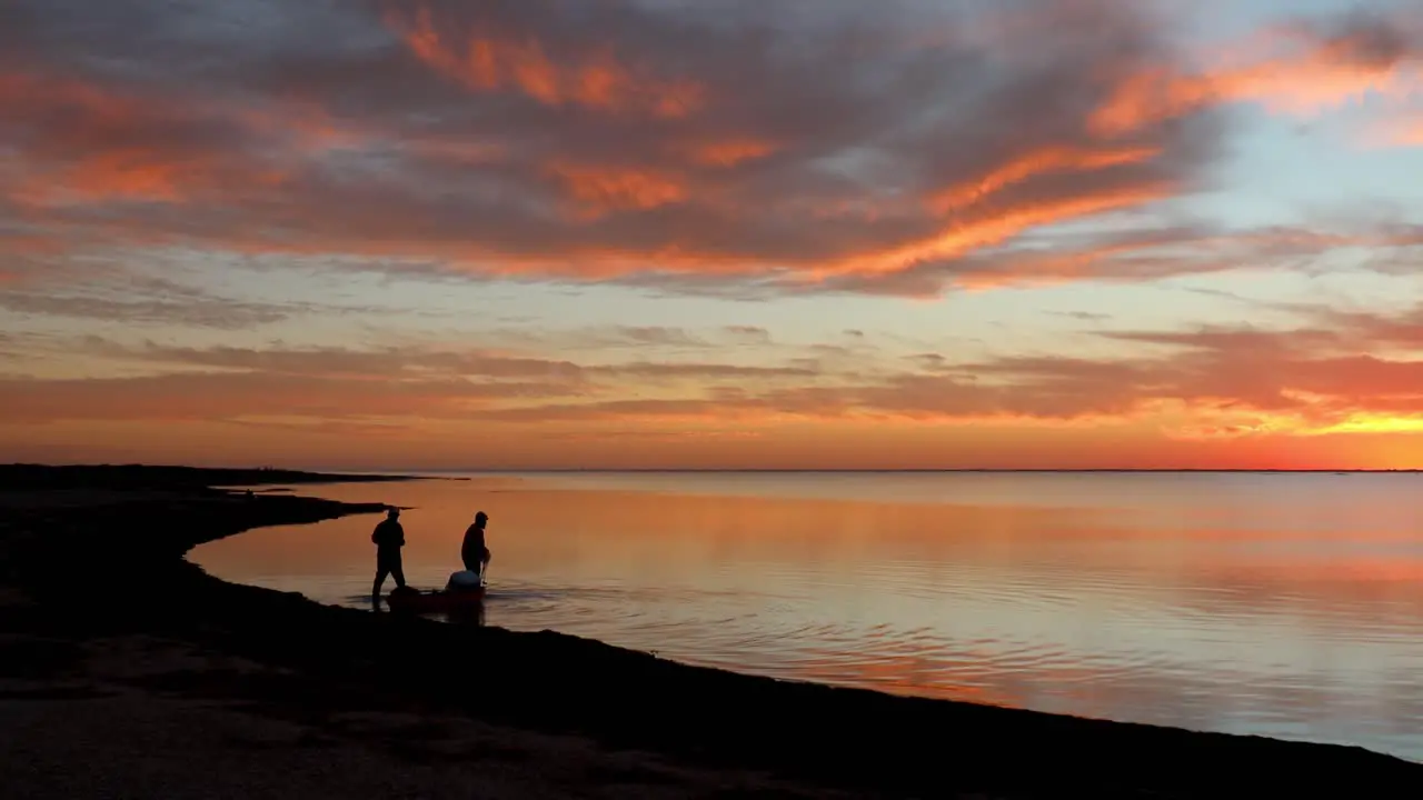 Two fishermen wade into tranquil Laguna Madres estuary while towing gear in a kayak during a gorgeous sunset