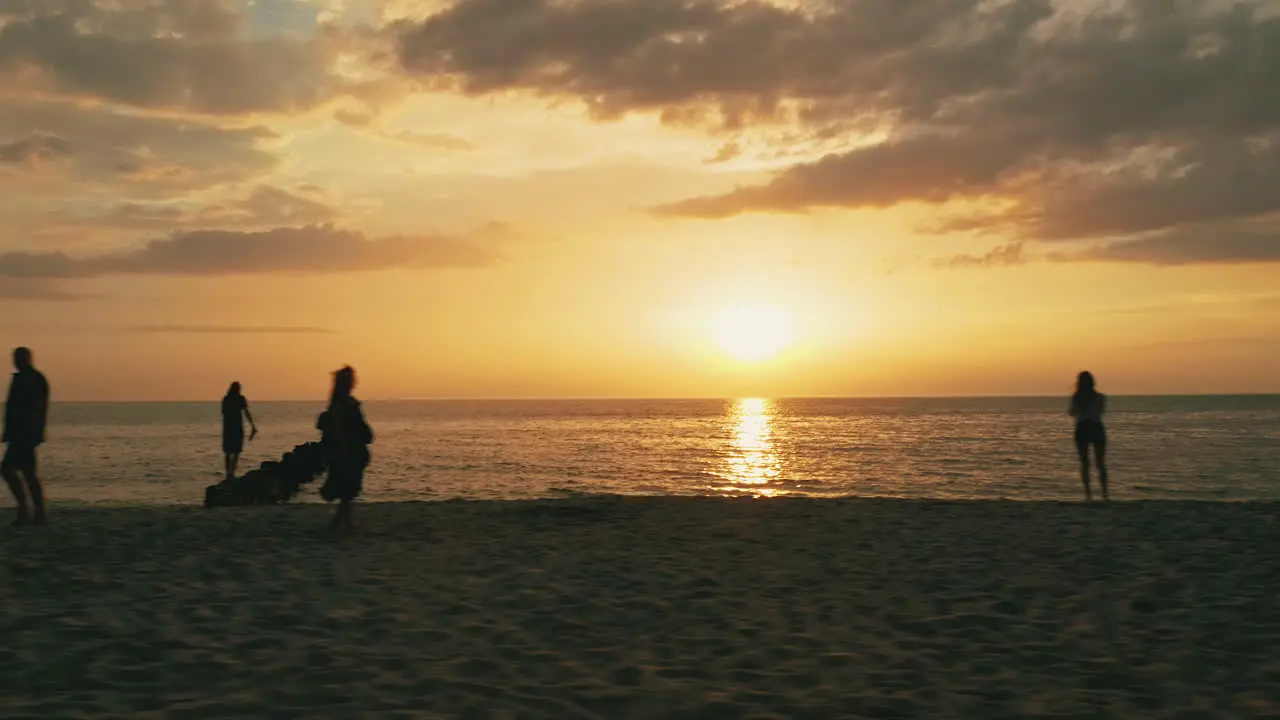 Low sideways flying drone shot of people walking on the beach during sunset