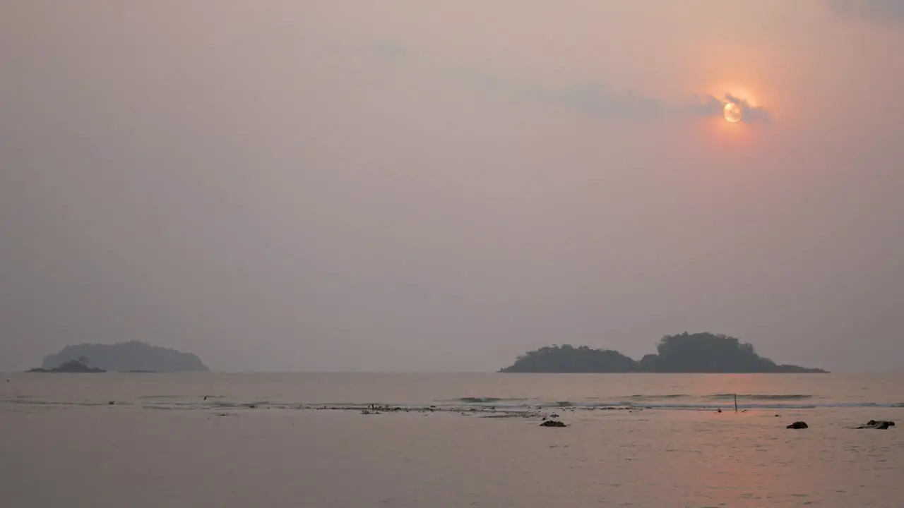 Hazy Red Sunset Behind Small Clouds Over Ocean And Hills