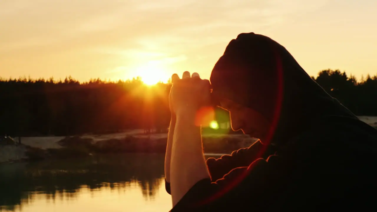 A young man in a hood prays at sunset 2