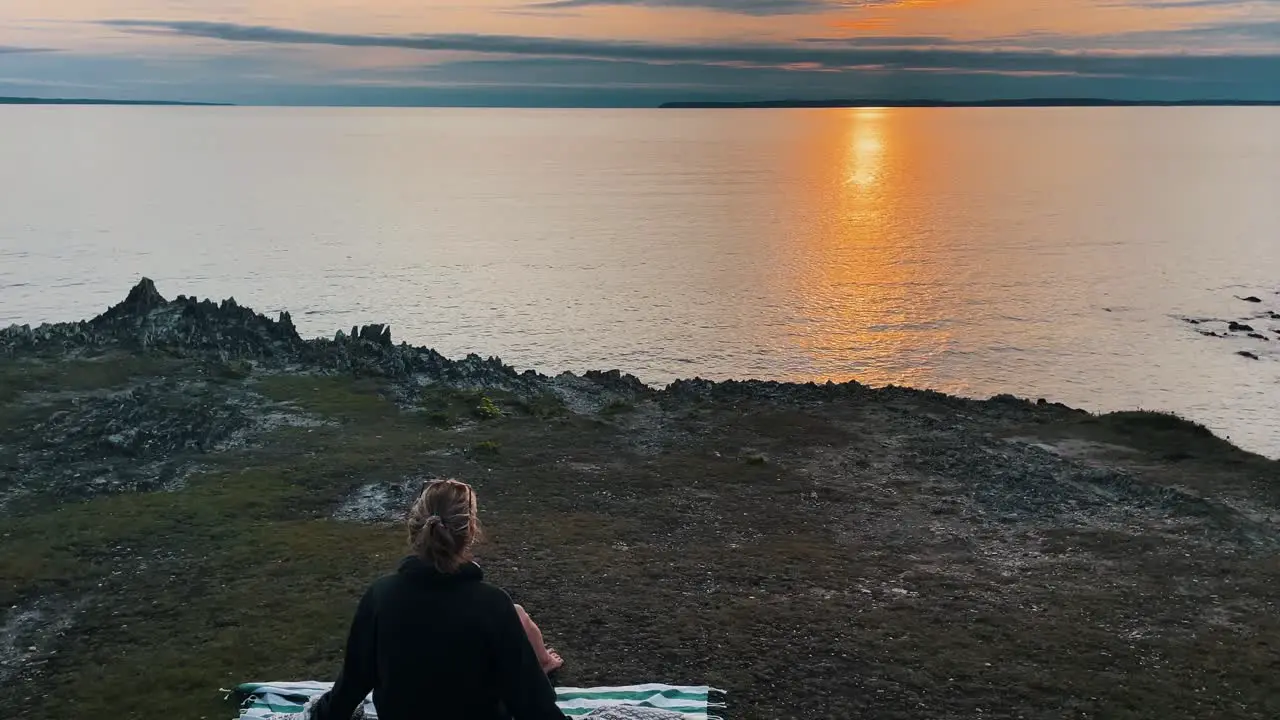 Aerial of dreamlike ocean scenery with young attractive woman throwing blanket over herself during sunset in Brittany France