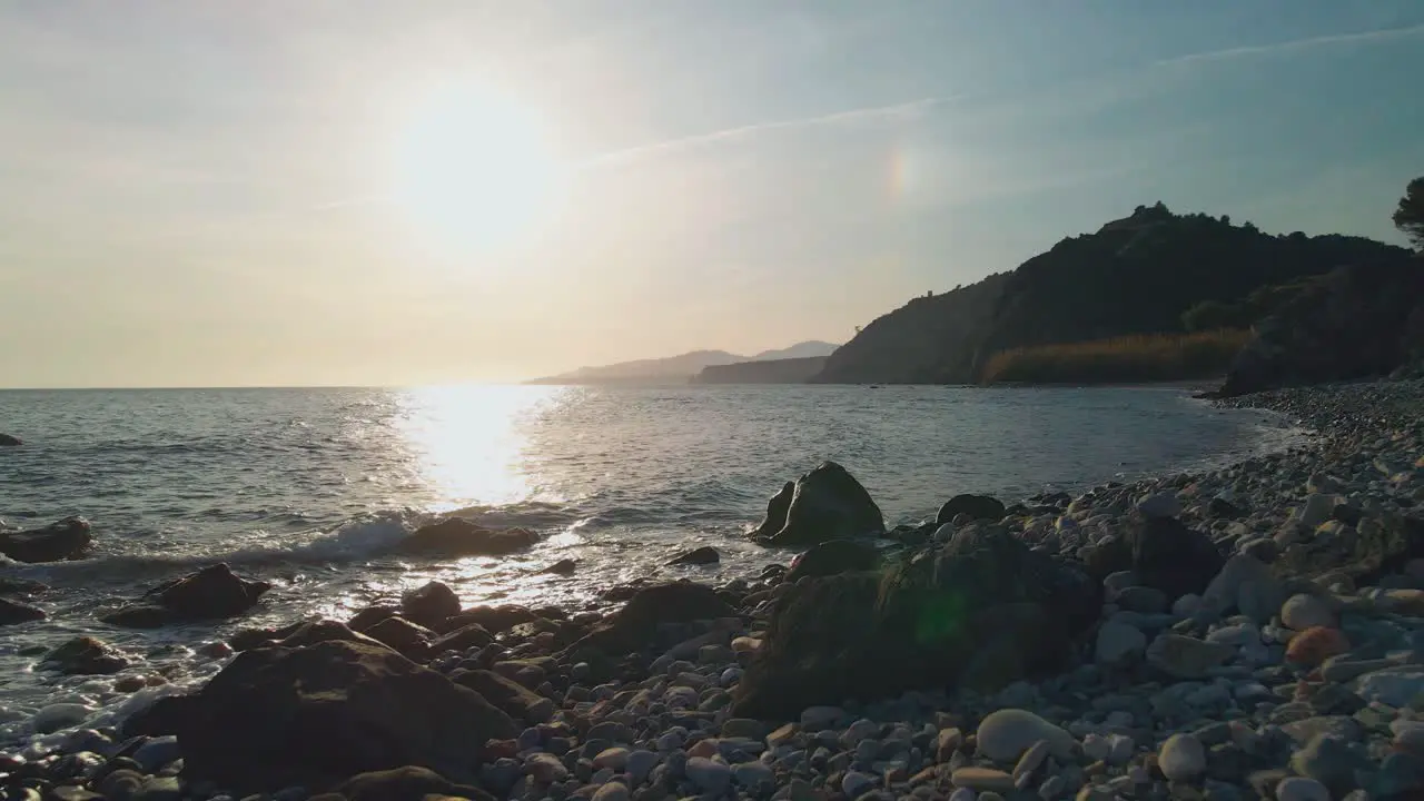 Drone moving backwards at an empty rocky beach during sunset