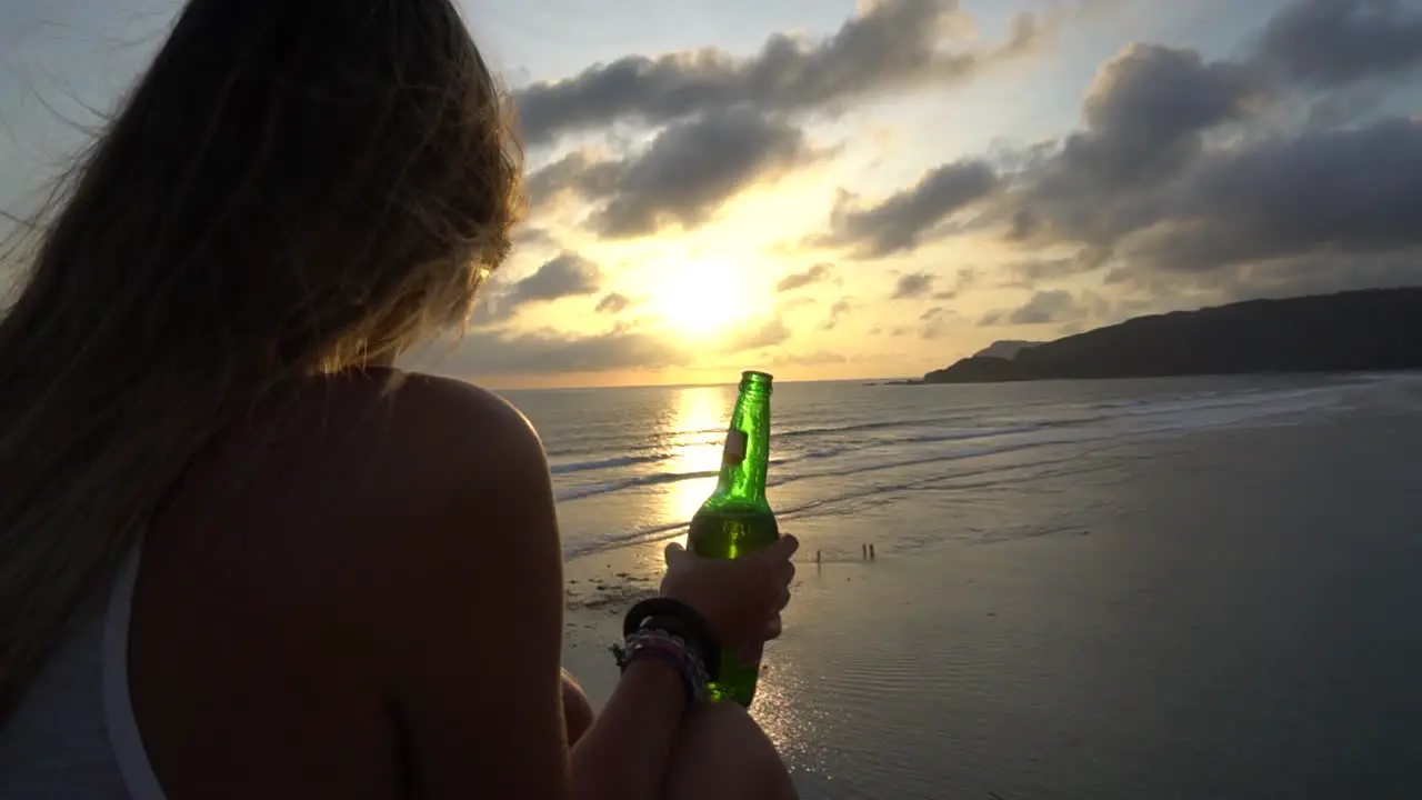 Long haired girl sitting on the beach in windy evening with a beer in her hand and enjoying the sunset in Indonesia Lombok island