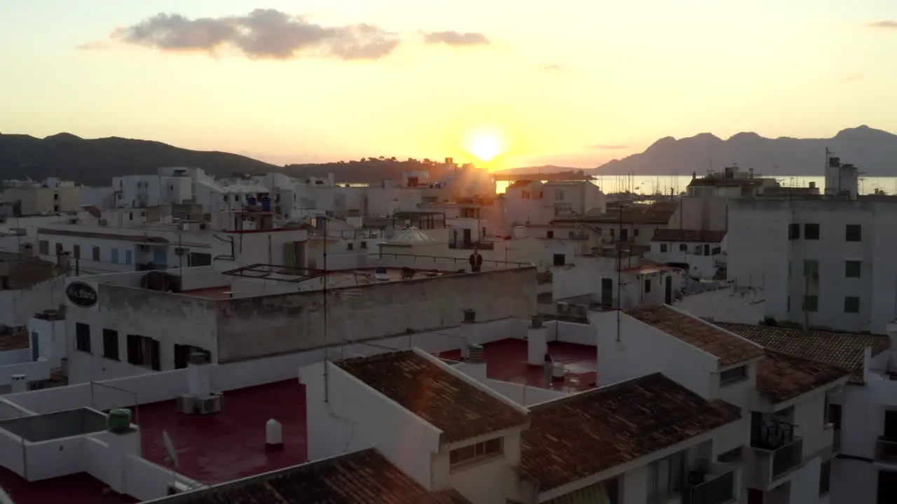 AERIAL Guy standing on roof of Small Townhouse with Port on Tropical Island with Boats and Ocean at Sunrise with Mountains in Background Vacation Travel Sunset