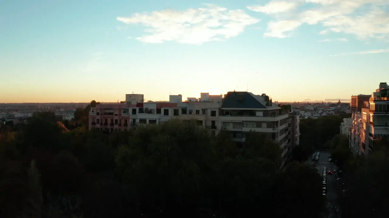 Forwards fly above trees in park revealing apartment houses and setting sun above city