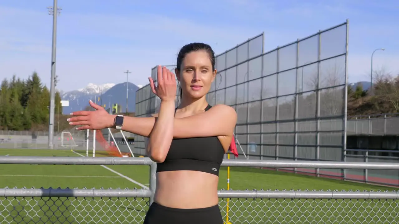 Young athletic woman stretching arm before exercising outdoors