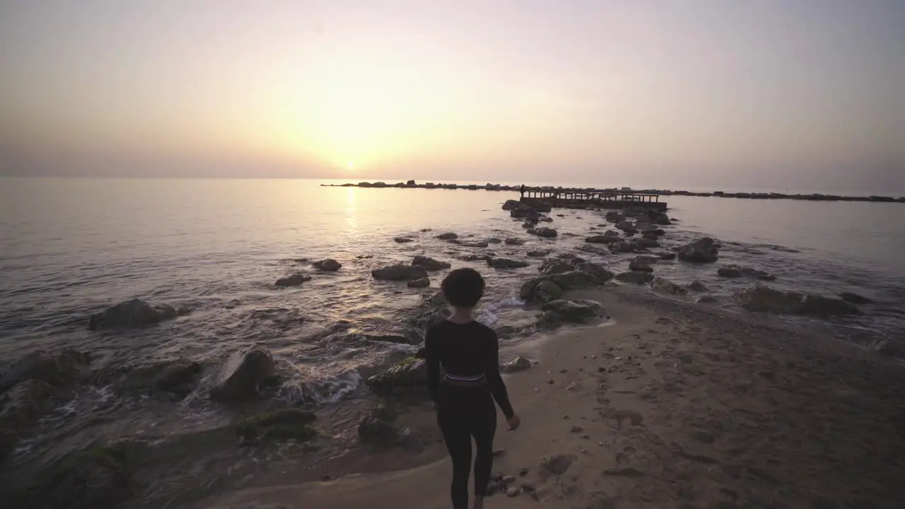 Black afro American tourists woman walking on the rocky beach of Barcelona spain famous tourist destination during epic sunset over the sea