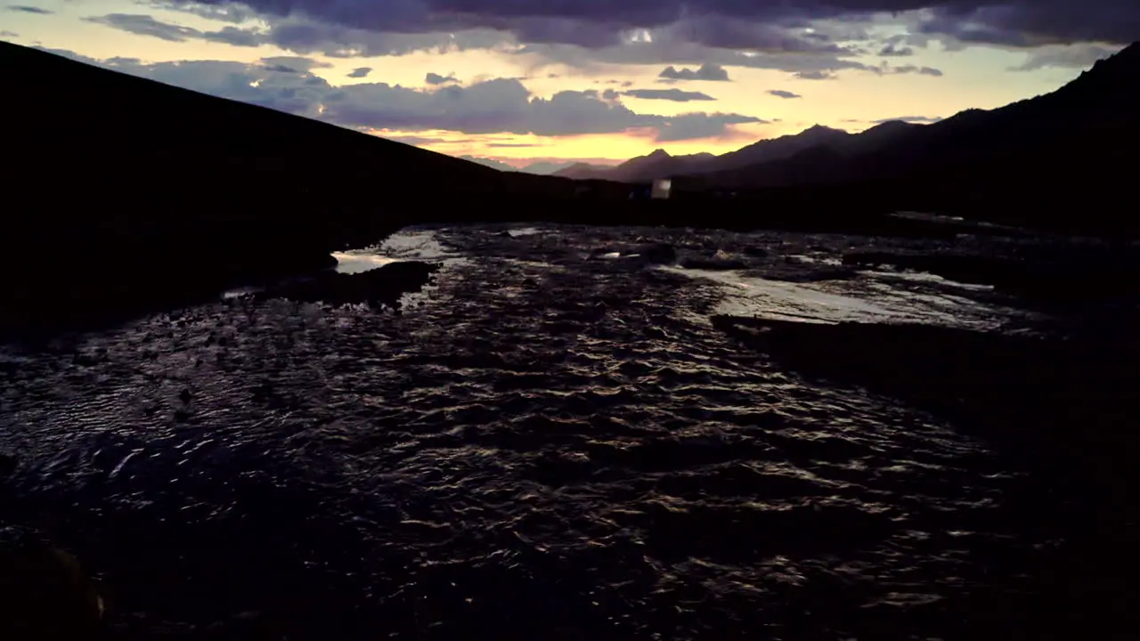 Tilt-up dark shot from a river to a sunset scene over a mountain range in the Himalayas