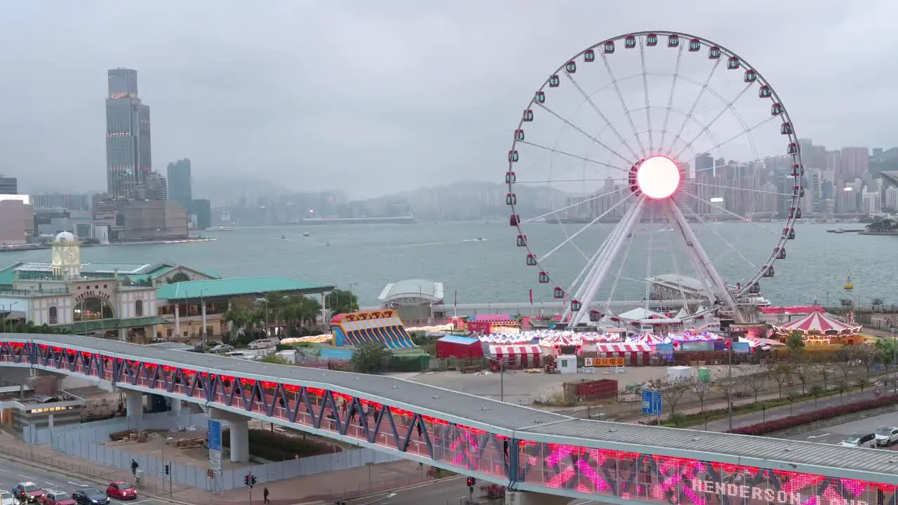 A pedestrian bridge is decorated with Chinese red lanterns as people walk through it while in the background there is a Ferris wheel in Hong Kong