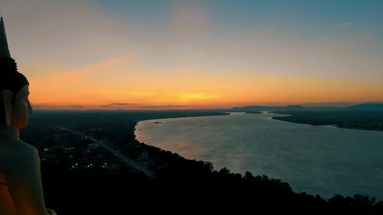 4k footage of a stunning sunset over the mighty Mekong river in Laos peacefully observed by a big Buddha statue