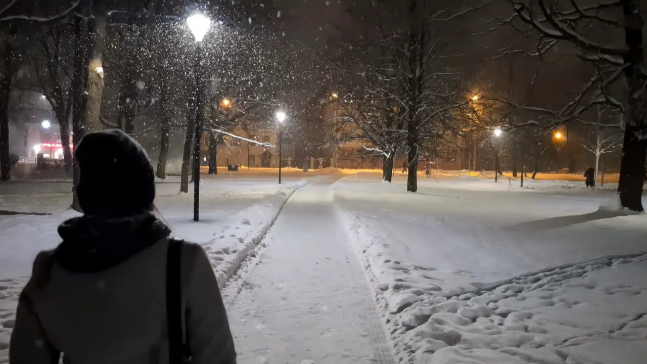 Women walking alone at night on snow path in urban park of Riga Latvia