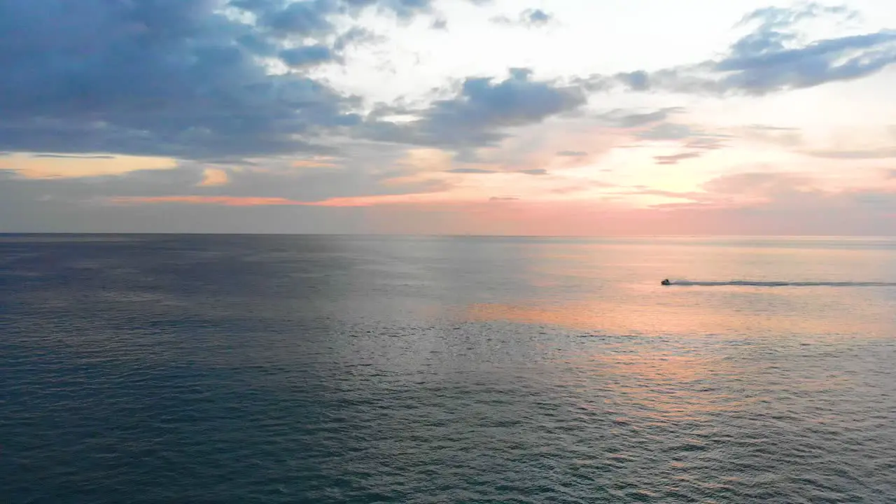 Strafing aerial drone shot of a beautiful sunset across the Andaman Sea horizon with a jetski passing by located at the tip of Phuket in Southern Thailand