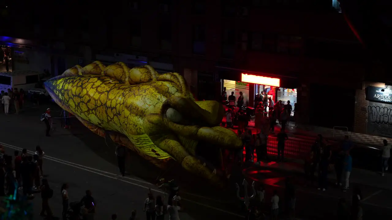 Workers attempting to repair a street eel balloon at nighttime with an onlookers audience