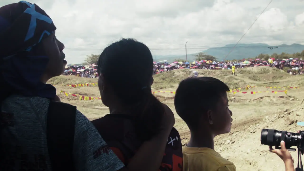 A family of onlookers watch in awe as multiple dirt bikes speed thru up close at the motocross competition